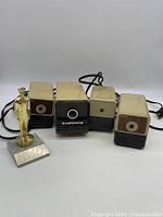 Four vintage Hunt Boston electric pencil sharpeners grouped with an award figurine on pedestal.