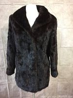 Front view of the dark brown mid-length coat jacket with wide lapel collar and long sleeves, showing plush fur texture.