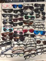 Top view of multiple rows of assorted sunglasses and eyeglass frames arranged flat showing diverse styles, colors, and shapes.