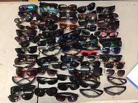 Photo showing a large collection of sunglasses of various styles and colors arranged on a surface.