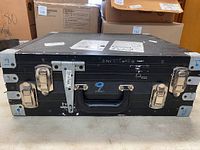 Front view of black hard case showing metal latches, handle, and wear marks