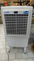 Front view of white Cool-A-Zone CoolBox portable evaporative air cooler on caster wheels showing vent and control panel.