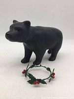 Front and side view of the matte black bear figurine standing on flat surface with holly collar in front
