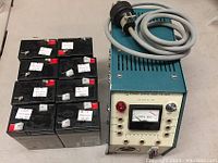 View of the eight SigmasTek SP6-4.5 batteries stacked in two rows next to the Feedback Power Supply Unit PS 150E along with its power cord.