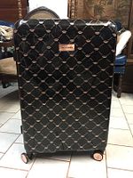 Front view of black Juicy Couture suitcase showing the branded nameplate and diamond pattern with crown logos.