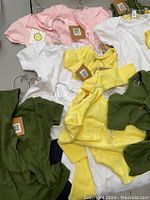 Multiple baby bodysuits in pink, white, yellow, and green colors, laid out with tags and hangers, new condition.