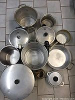 Top view showing all pots, saucepans, lids, and teapot arranged on floor tiles