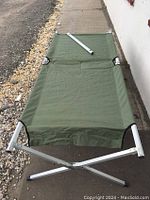 Full length view of green fabric camping cot unfolded, showing metal frame and fabric surface.