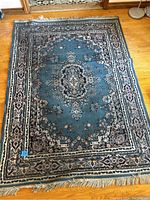 Full view of the rectangular 5x7 area rug with blue background and detailed border pattern, placed on wooden floor.