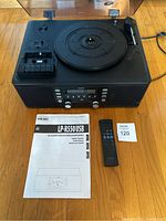 Front top view of TEAC LP-R550USB device with turntable, control panel, dust cover, remote control, and manual laid on wooden floor