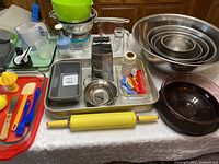 Photo of entire baking lot showing mixing bowls, rolling pin, baking trays and assorted baking tools spread on table.