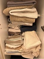 Folded neutral color bath towels stacked on a shelf, showing various sizes and fabric textures.