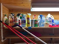 Shelf with assorted cleaning spray bottles and liquids in various plastic bottles.
