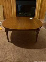 Front view of a round vintage wooden coffee table placed on carpet in front of a fireplace.