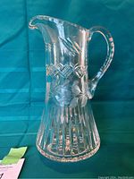 Front and side view of a clear cut glass pitcher with cornflower design and vertical cut lines at base.