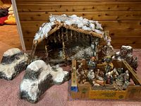 Overview of nativity scene with stable, box of figurines and mountain props on carpeted floor.