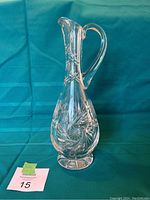 Full view of the tall clear crystal pitcher with handle and etched pinwheel pattern on a blue background.