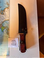 Full view of the knife sheathed on a white surface with part of a world map in background.