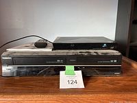 Front view of the Toshiba DVD Video Cassette Recorder and Blu-ray Disc Player stacked on a wooden surface