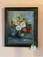 Frontal view of framed floral oil painting featuring colorful bouquet in vase against blue-gray background.
