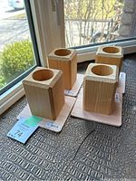 Four wooden furniture risers arranged in two rows, showing hollowed top for furniture leg fitting.