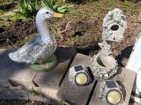 Lot overview showing the weathered goose figurine, the decorative birdhouse planter, and the pair of solar rock lights on a stone ledge outdoors.