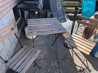 Photo showing the full IKEA bistro set with one table and two chairs arranged outdoors on a concrete surface near a wall.