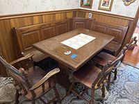 Full view of wood dining table, L-shaped corner bench and four chairs around set in corner against wood paneled walls.