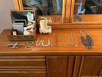 Wide view of jewelry, watches, decorative items arranged on a wooden dresser showing various necklaces, bracelets, and boxes.