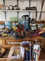 Wide shot showing workbench with assorted hand tools, drills, gloves, and storage items spread out.