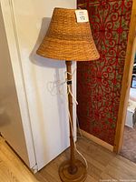 Full view of MCM floor lamp showing wooden base and woven wicker lampshade with attached white electrical cord.
