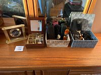 Photo of entire collection showing brass Junghans clock, wooden floral jewelry box, multiple eyeglass cases, black wallet, and small box with pins.
