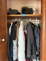 Photo showing men's jackets and rain pants hanging on rod in closet