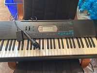 Full view of Casio CTK-2100 keyboard on a chair with wired microphone placed on keys, showing buttons, control panel, and keys.
