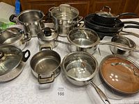 Full view of the lot showing an assortment of pots, pans, lids, and a steamer on a table.