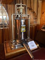 Full view of the Power Fist sausage stuffer showing stainless steel cylinder mounted on wooden base with metal supports and crank handle.