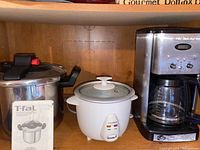 Shelf with three appliances: T-Fal pressure cooker, Homemax rice cooker, and Cuisinart coffee maker
