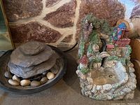 Photo showing both tabletop water fountains side by side on a stone surface against a stone textured wall.