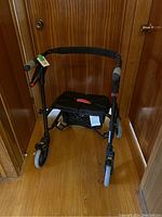 Front view of black Nexus foldable walker showing padded seat, frame, wheels and hand brakes.