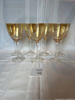 Front view of seven amber tinted wine glasses arranged in a row showing their shape and size.