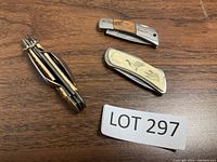 Three small folding pocket knives on wood surface, different handles and designs