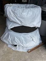 Photo of 4 tires stacked in pairs and covered partially with white plastic sheeting.