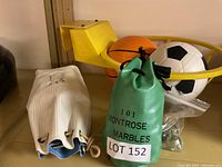 Yellow plastic basketball hoop toy with mini basketball and soccer ball next to two bags labeled '101 Montrose Marbles'