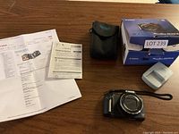 Canon digital camera, charger, black carrying case, box, and documentation arranged on wooden table