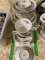 View of assorted stacked china pieces including plates, bowls, teacups, and saucers with floral pattern and gold trim.