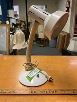 White desk lamp shown on wooden surface with gooseneck and dome-shaped metal shade, toggle switch on base, power cord wrapped beside base