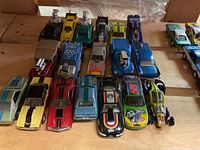 Top down view showing three rows of die cast cars arranged on a wooden surface, showcasing the variety in colors and styles including several with exposed engines and racing motifs.