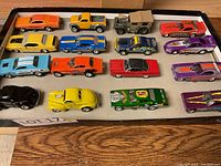 Top-down view of all 16 die cast and model cars arranged in a box on a wooden table