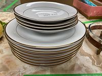 Stack of white porcelain dinner plates with gold trim, showing side view of the plates.