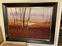 Framed art with bare trees and reddish-brown ground, dark wooden frame with metal inner edge.